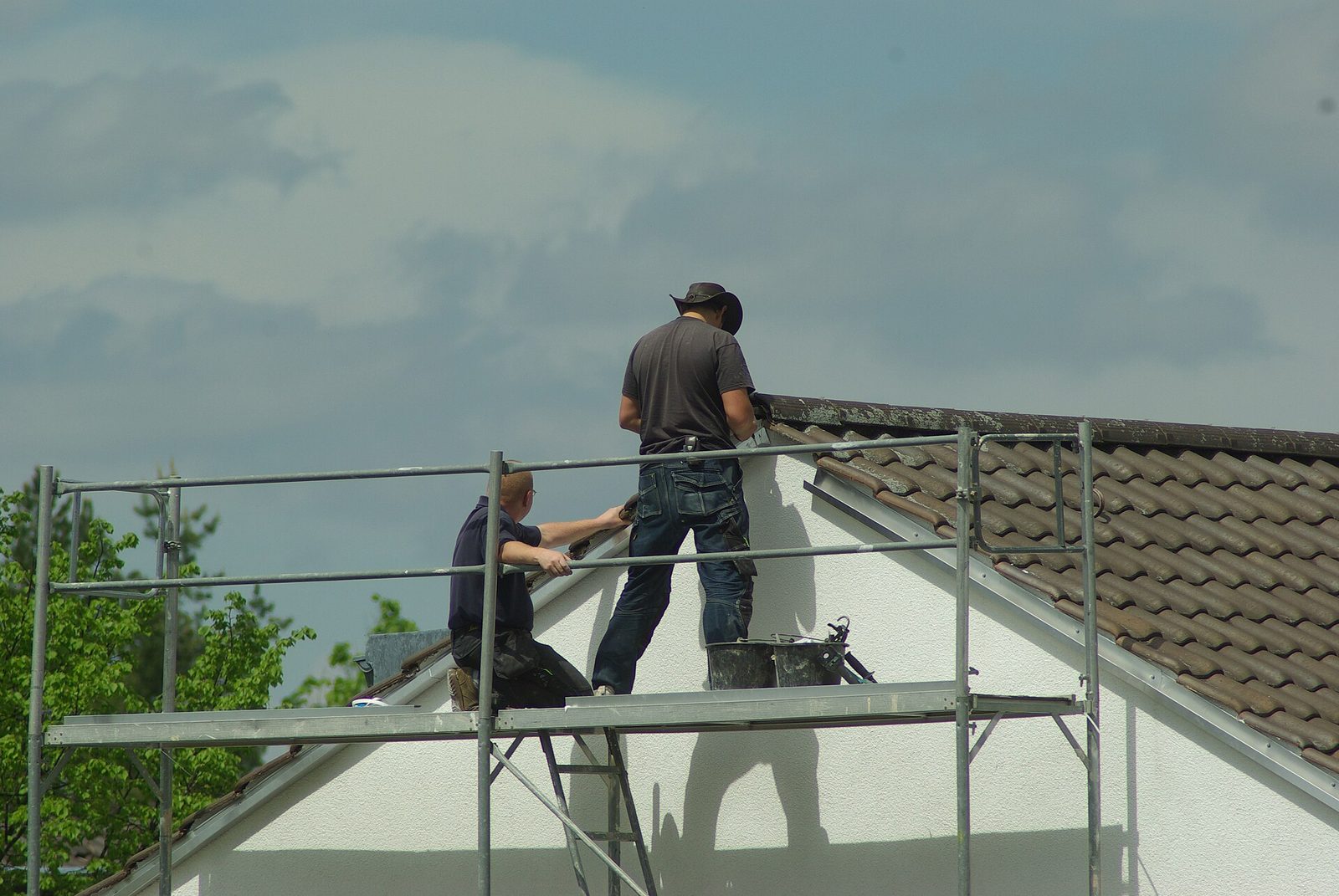 Twee werklieden op een stelling bij de dakrand van een witte gevel