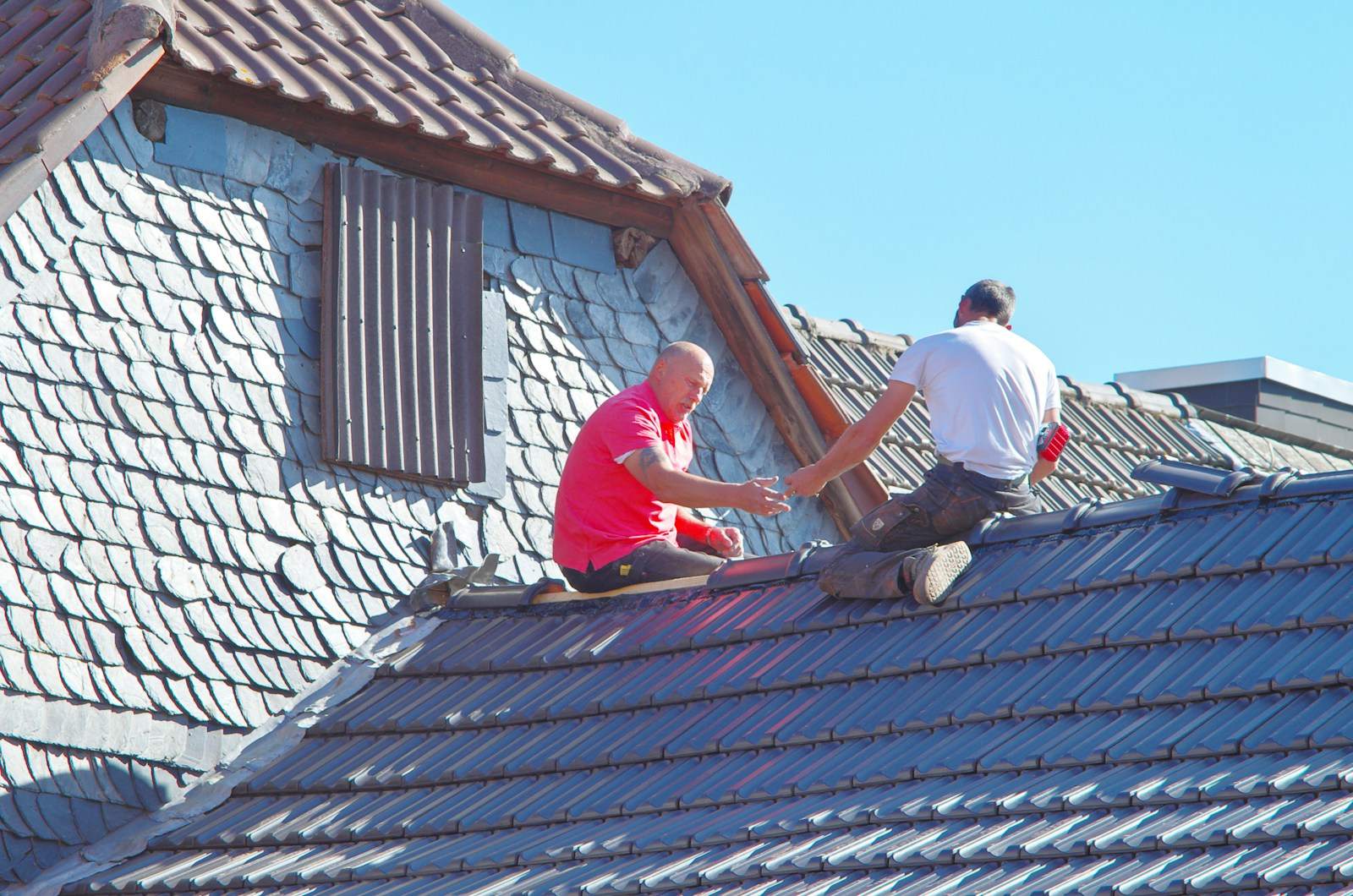Twee mannen werken aan een dak naast een dakkapel